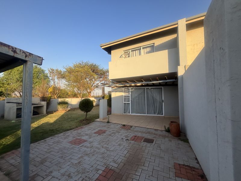 Rear view of the townhouse featuring a paved patio area, built-in braai, and a balcony accessible from the upper level.