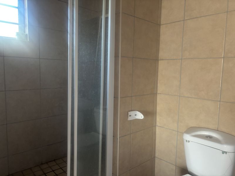 A functional bathroom featuring a shower enclosure and toilet, finished with neutral wall and floor tiles. Requires minor repairs to fixtures.