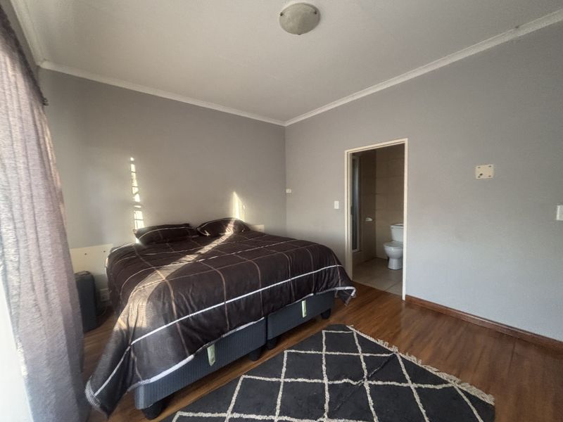 A bedroom featuring laminate flooring and an en-suite bathroom, requiring minor cosmetic updates to the wall finishes and electrical fixtures.