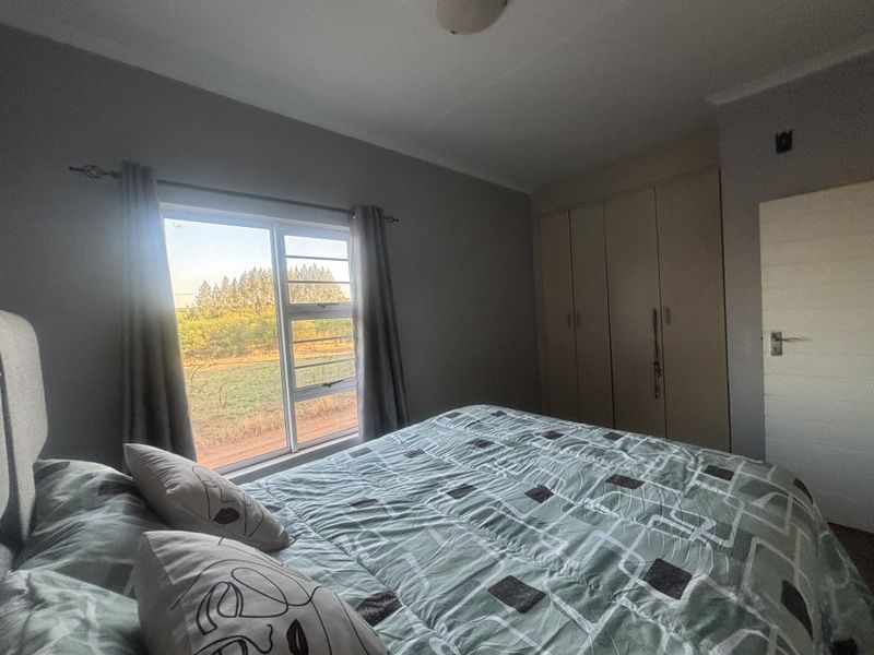A functional bedroom featuring built-in cupboards, neutral wall finishes, and a window providing natural light and views of the surrounding landscape.