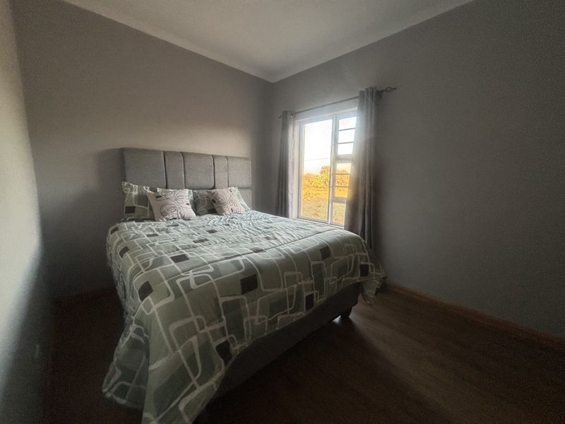A well-maintained bedroom featuring laminate flooring, neutral wall tones, and a window with security burglar bars allowing for natural light.