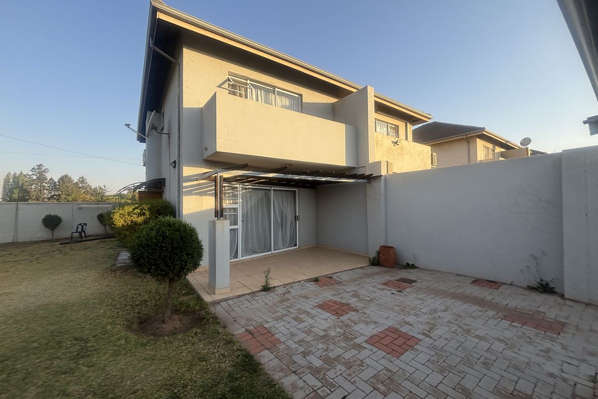 Rear view of the townhouse featuring a paved patio area, a covered pergola, and an upper-level balcony overlooking the private garden space.