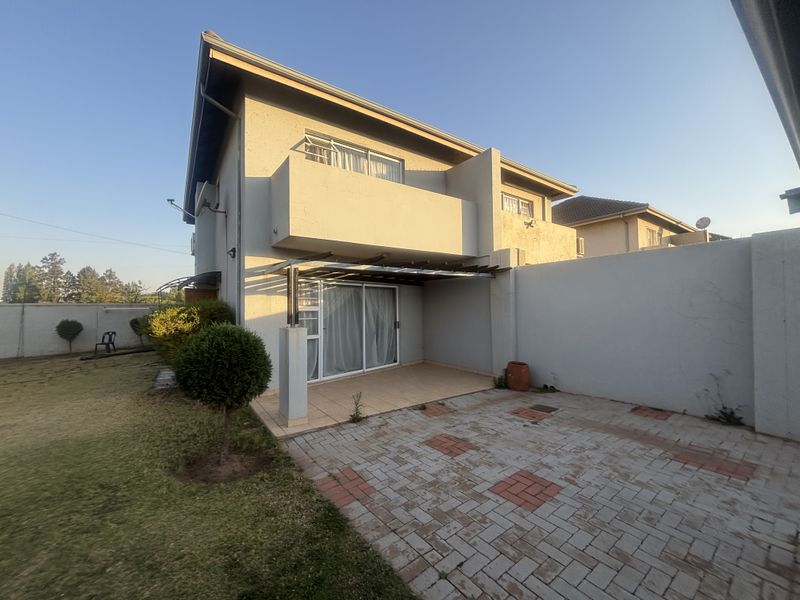 Rear view of the townhouse featuring a paved patio area, a covered pergola, and an upper-level balcony overlooking the private garden space.