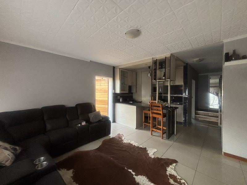 Open-plan living area featuring a kitchen with breakfast bar, tiled flooring, and textured ceiling tiles, creating a functional combined living and dining space.