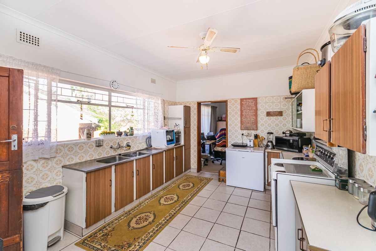 A functional kitchen featuring dated wall tiles, laminate cabinetry, double stainless steel sink, and ceramic floor tiles, offering potential for modern renovation.