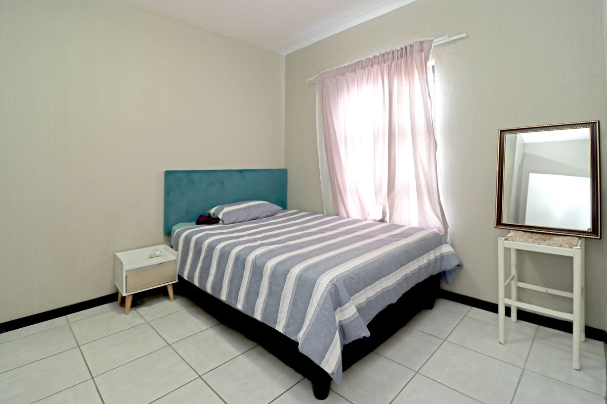 A functional bedroom featuring neutral wall finishes, tiled flooring, and a window with a curtain rail.