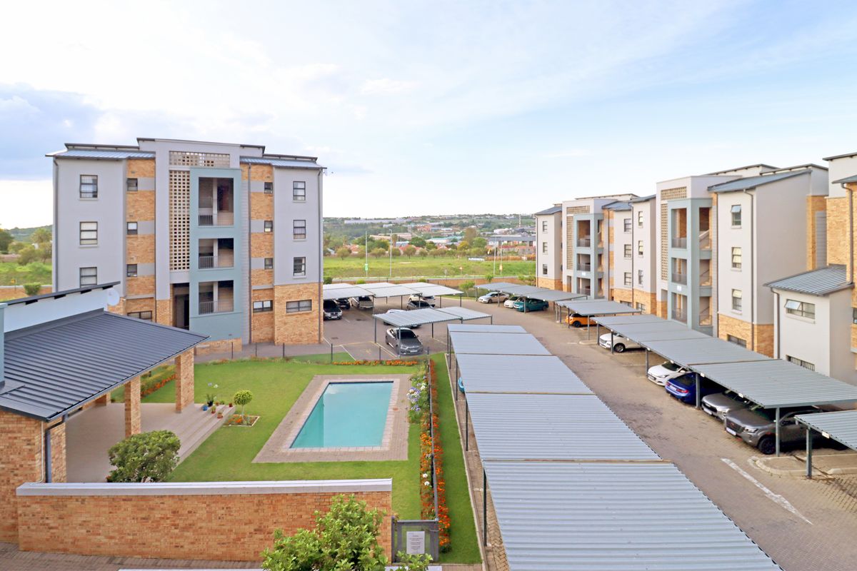 Aerial view of an apartment complex featuring a swimming pool, landscaped garden, and extensive covered parking bays for residents.