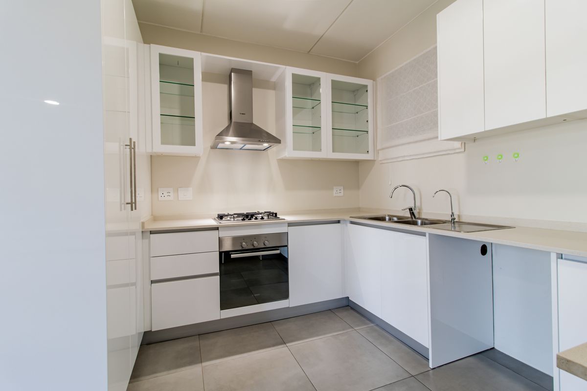 Modern kitchen featuring white cabinetry, stone countertops, stainless steel appliances including a gas hob and extractor fan, and neutral tiled flooring.