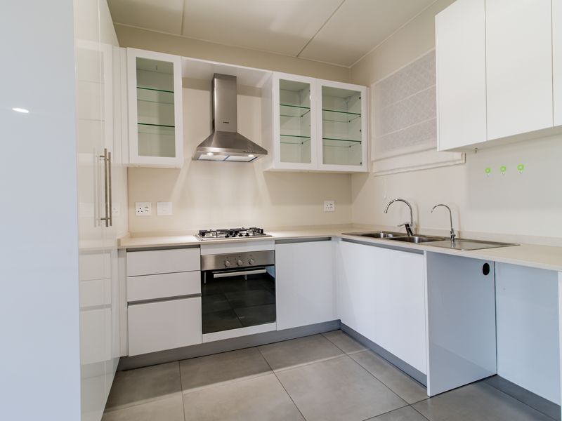 Modern kitchen featuring white cabinetry, stone countertops, stainless steel appliances including a gas hob and extractor fan, and neutral tiled flooring.