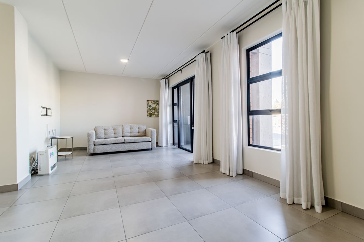 A bright and spacious living area featuring large windows, neutral tiled flooring, and a sliding glass door leading to an outdoor space.