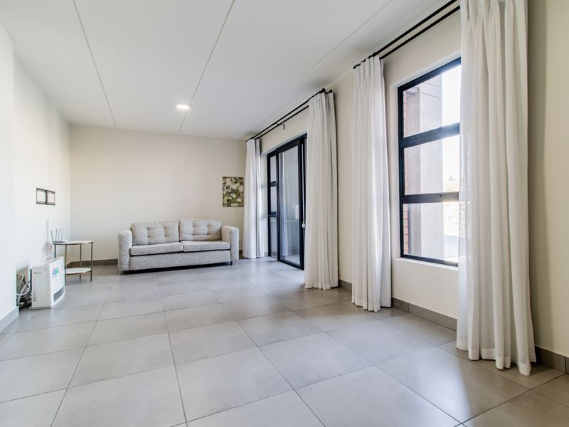 A bright and spacious living area featuring large windows, neutral tiled flooring, and a sliding glass door leading to an outdoor space.