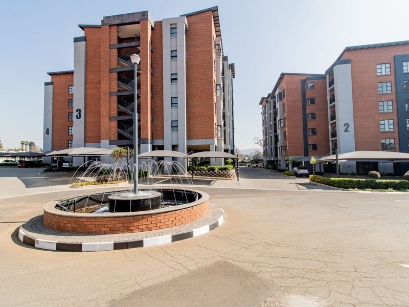 Exterior view of a modern apartment complex featuring brick facades, a central fountain, and covered parking bays.
