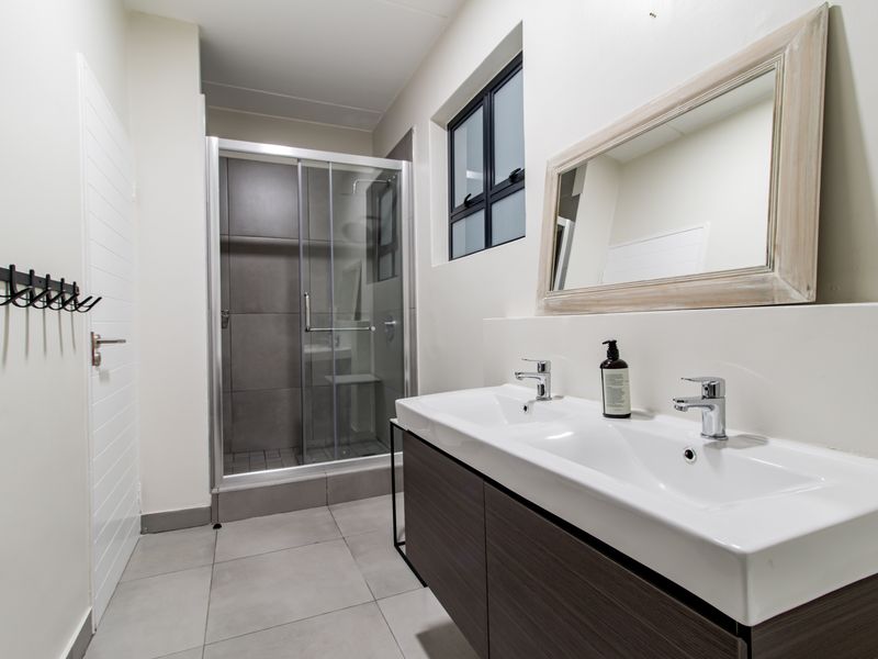 Modern bathroom featuring a double vanity with integrated sinks, a glass-enclosed shower, and neutral floor tiling.