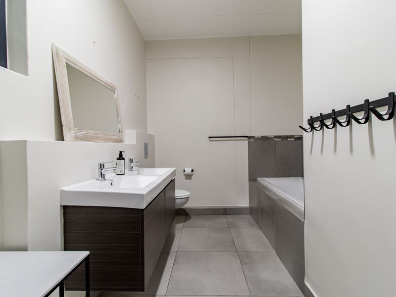 Modern bathroom featuring a double vanity, built-in bathtub, and neutral tiled finishes, providing a clean and functional space.