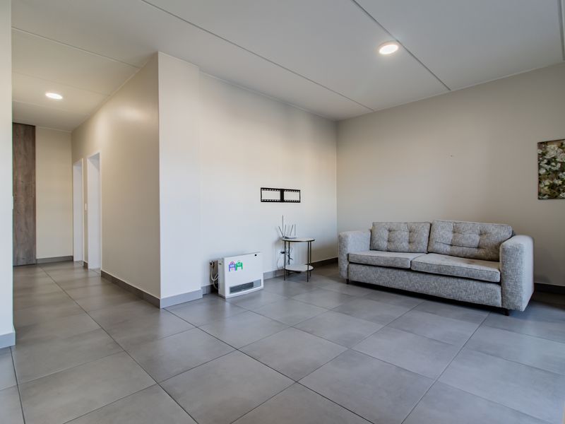 A bright and spacious living area featuring neutral tiled flooring, recessed ceiling lighting, and a wall-mounted heater.
