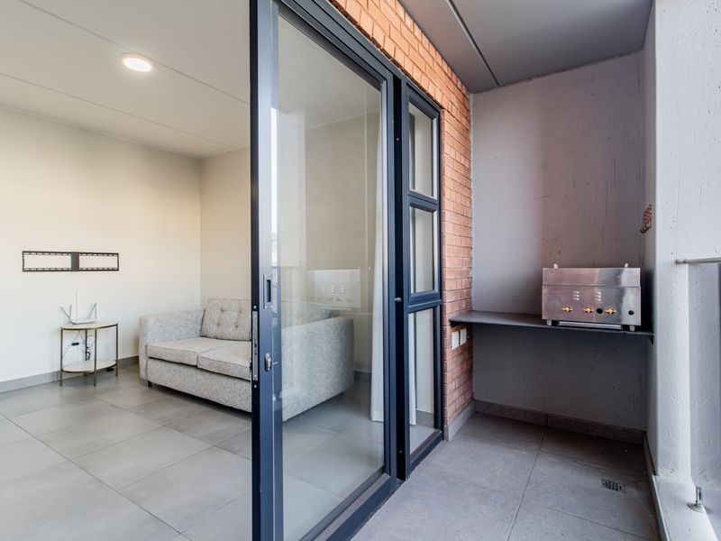 A modern balcony featuring a built-in braai, tiled flooring, and a glass balustrade, providing seamless access to the interior living area.