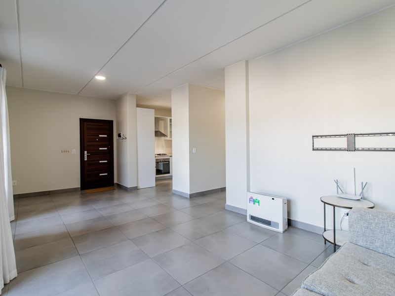 Spacious open-plan living area featuring neutral tiled flooring, recessed lighting, and a modern kitchen with built-in appliances and clean finishes.