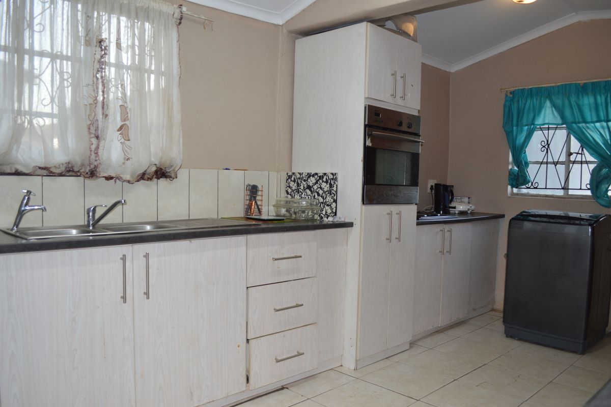 A functional kitchen featuring white built-in cabinetry, laminate countertops, a built-in oven, and tiled flooring with security bars on the windows.