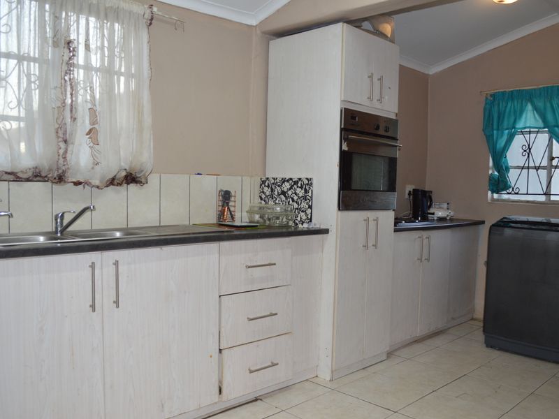 A functional kitchen featuring white built-in cabinetry, laminate countertops, a built-in oven, and tiled flooring with security bars on the windows.