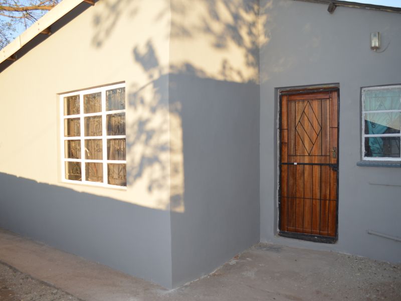 A view of the rear exterior facade featuring a timber door with a security gate and grid-style windows on a grey painted wall.