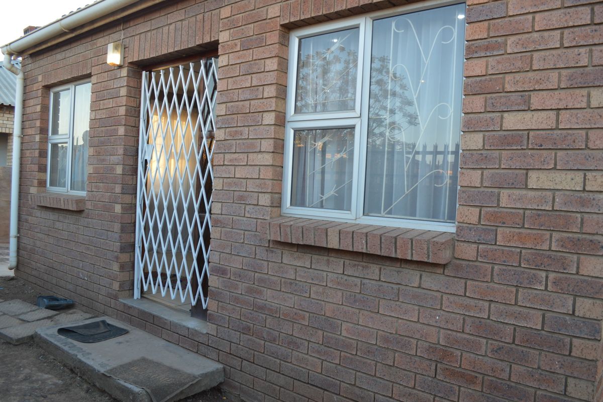 Exterior view of a face brick house featuring aluminium window frames, security bars, and a white security gate at the entrance.