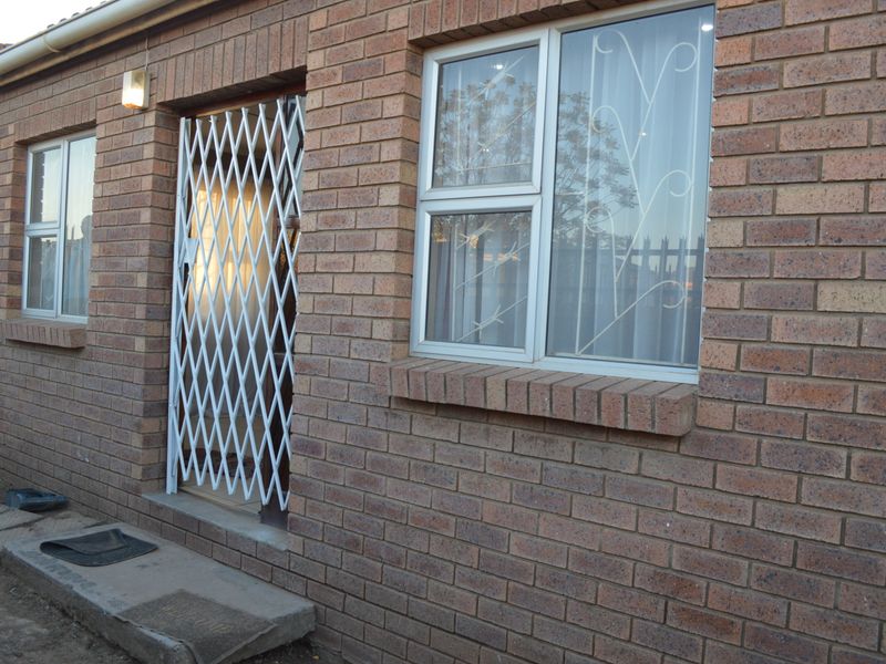 Exterior view of a face brick house featuring aluminium window frames, security bars, and a white security gate at the entrance.