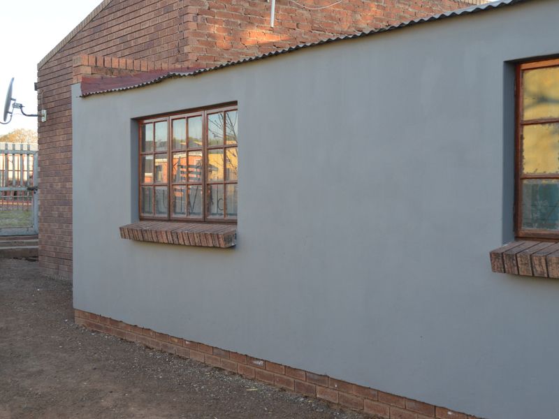 Rear exterior view of the property featuring a plastered wall, timber-framed windows with brick sills, and a brick facade section.