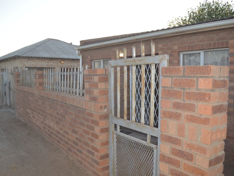 Front exterior view of a face brick house featuring a secure metal gate and perimeter fencing.
