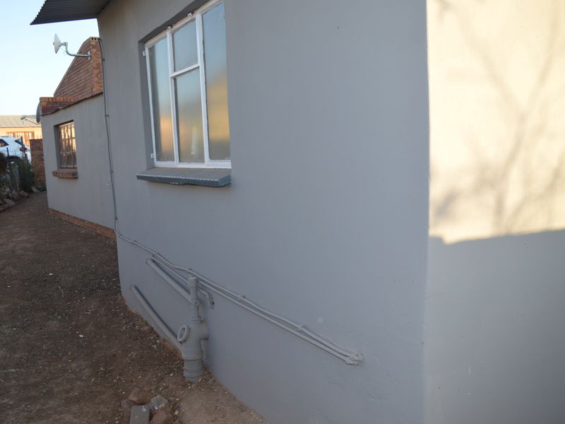 A view of the rear exterior wall featuring painted masonry, aluminium window frames, and exposed external plumbing infrastructure.