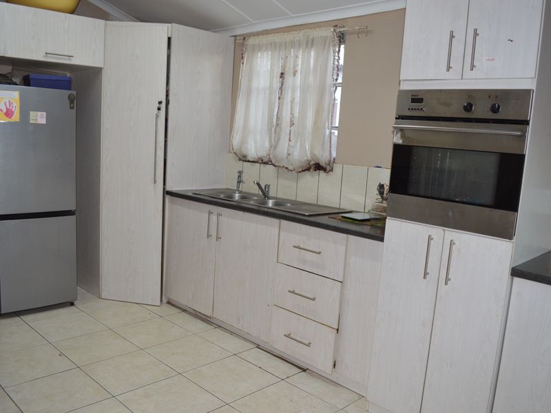 A functional kitchen featuring light-toned built-in cabinetry, laminate countertops, a stainless steel double sink, and a built-in oven with tiled flooring.