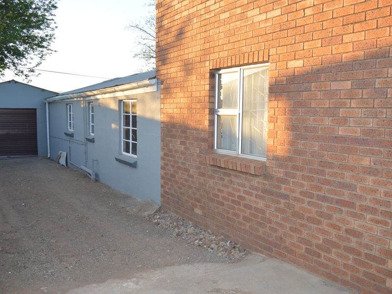 Side view of the property showing a brick and painted plaster exterior, aluminium windows with security bars, and a detached garage.