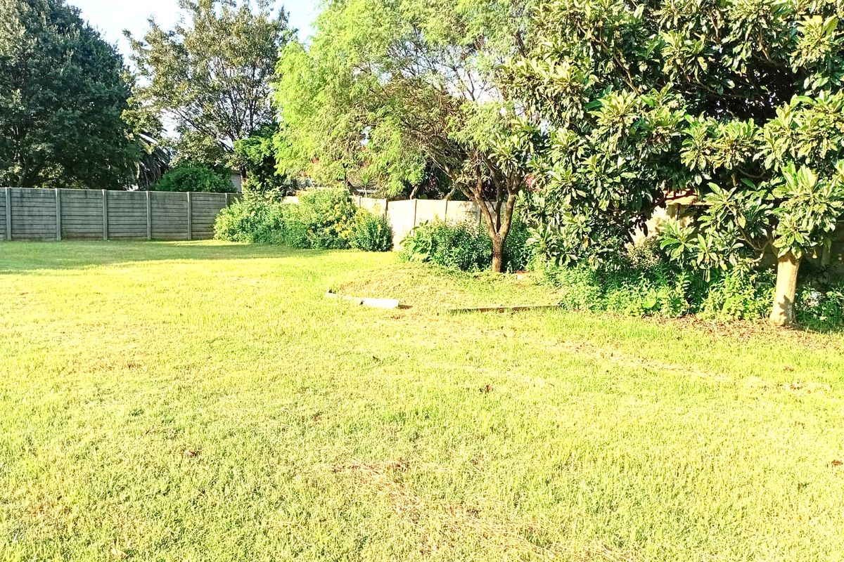 A spacious, level residential plot featuring established trees, lush green lawn, and perimeter concrete wall fencing.