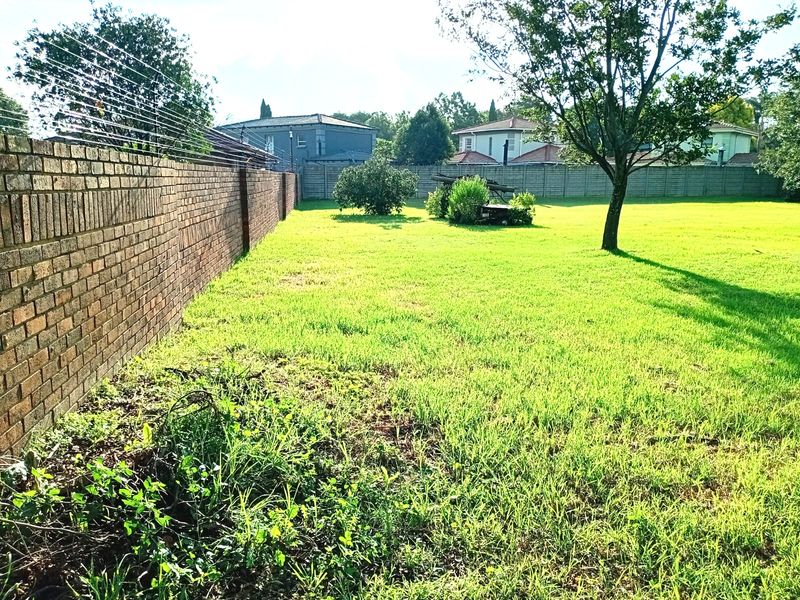 A spacious residential garden area featuring a brick perimeter wall with security fencing and established trees on a level grassed plot.