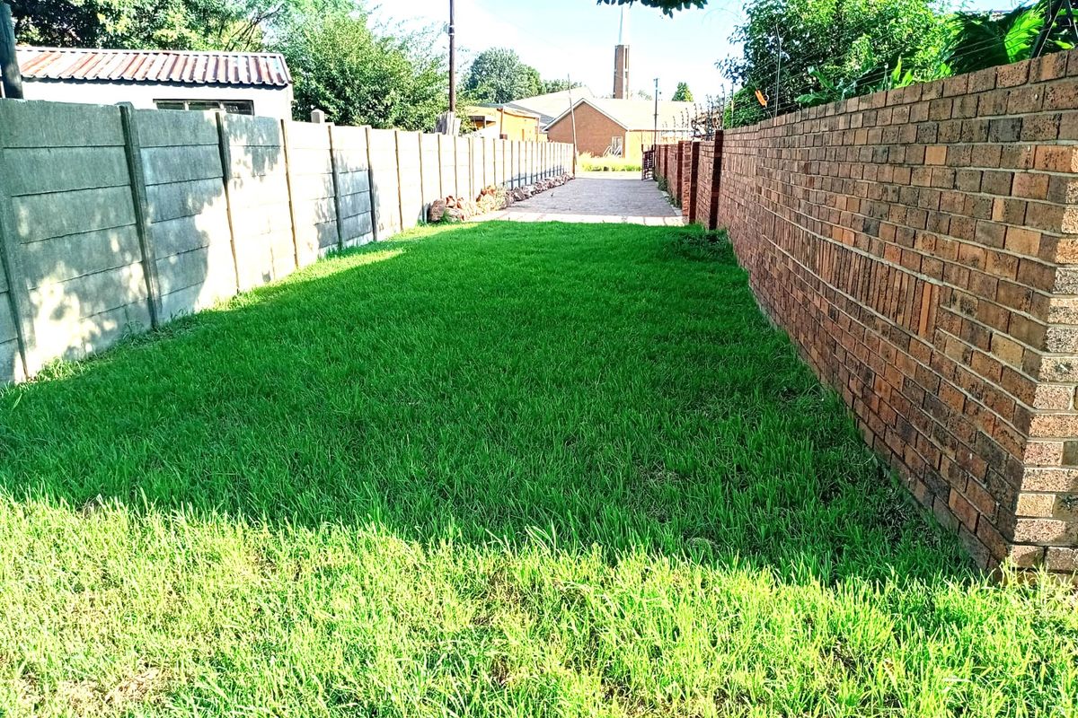 A narrow residential plot featuring a well-maintained grass lawn enclosed by a combination of face brick and precast concrete boundary walls.