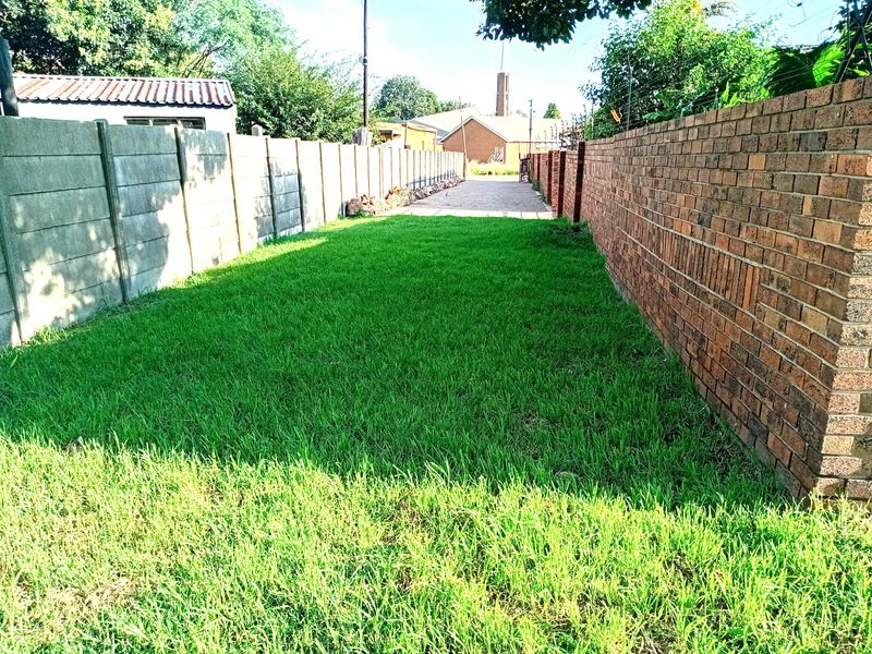 A narrow residential plot featuring a well-maintained grass lawn enclosed by a combination of face brick and precast concrete boundary walls.