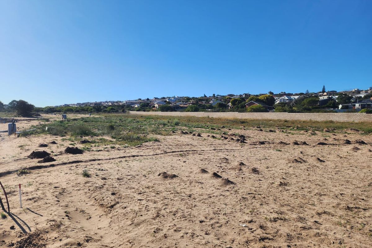 A vacant plot of land with sandy terrain and a boundary wall, offering a view of the surrounding residential neighborhood.