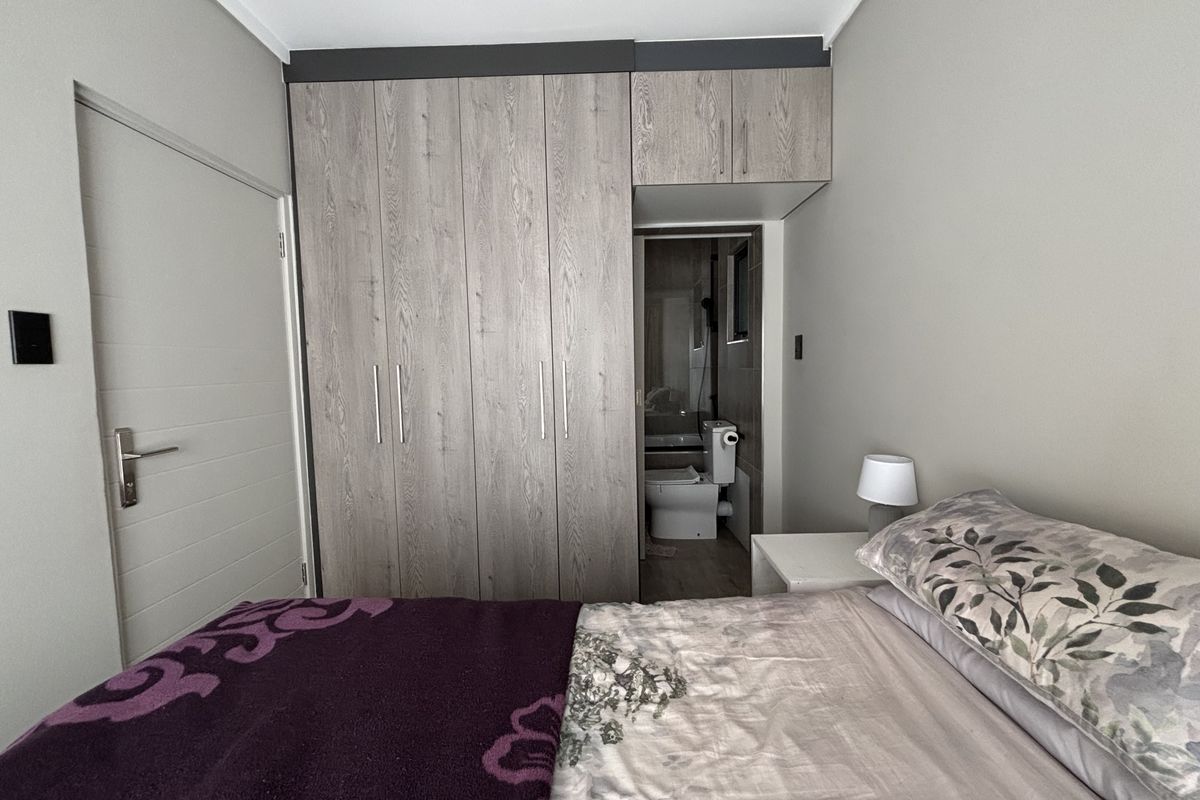 A well-maintained bedroom featuring modern wood-grain built-in cupboards with overhead storage and direct access to an en-suite bathroom.