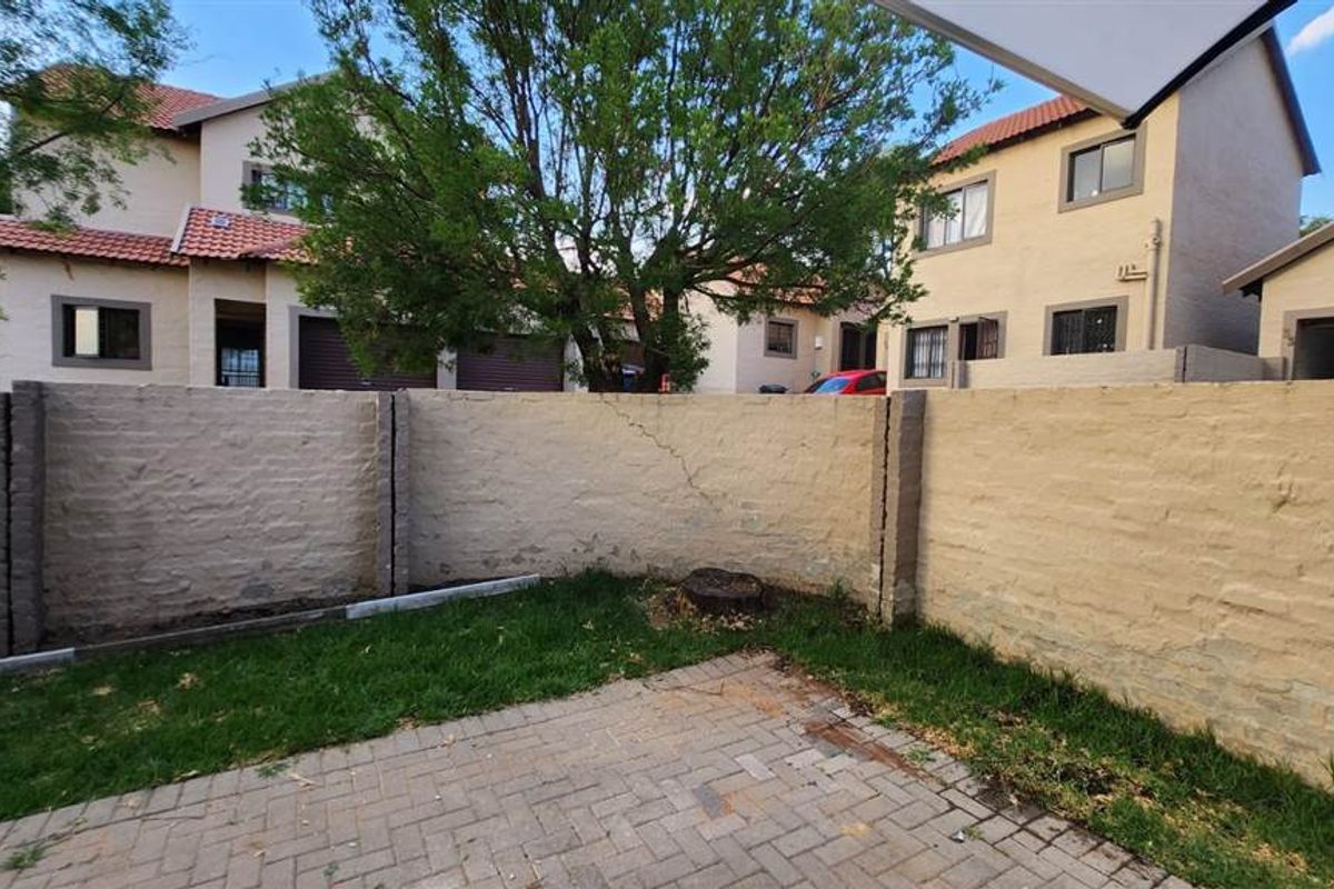 A private rear garden area featuring a paved patio, small lawn, and a boundary wall requiring maintenance.
