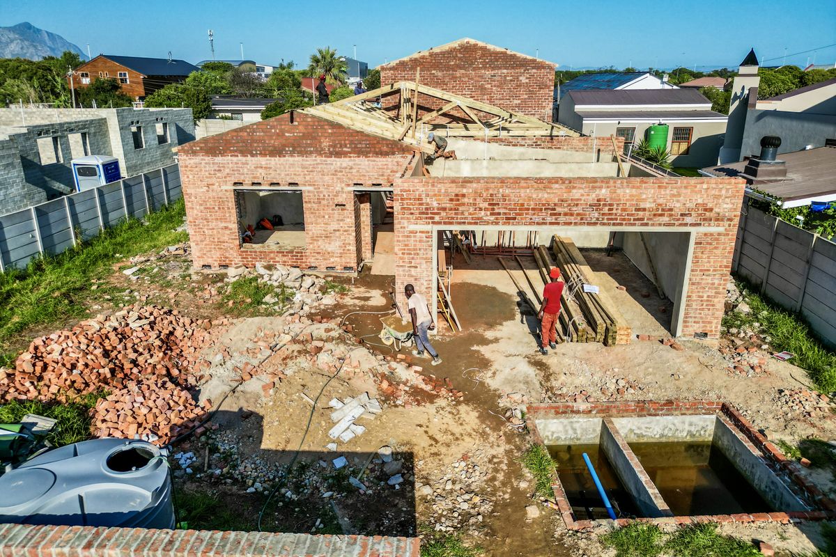 Aerial view of a residential property under construction, featuring exposed brick walls, timber roof trusses, and an unfinished site with a concrete basin.