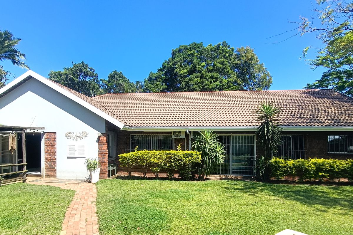 Rear view of a single-story brick house featuring a tiled roof, sliding glass doors with security bars, and a well-maintained garden.