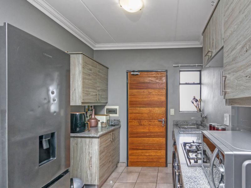 A functional kitchen featuring granite countertops, wood-look laminate cabinetry, a gas hob, and tiled flooring, providing a practical and well-maintained cooking space.