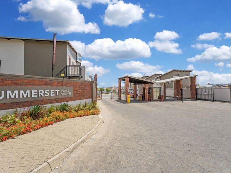 The entrance to Summerset Place Village featuring a secure gated access point, brick boundary wall, and paved driveway.