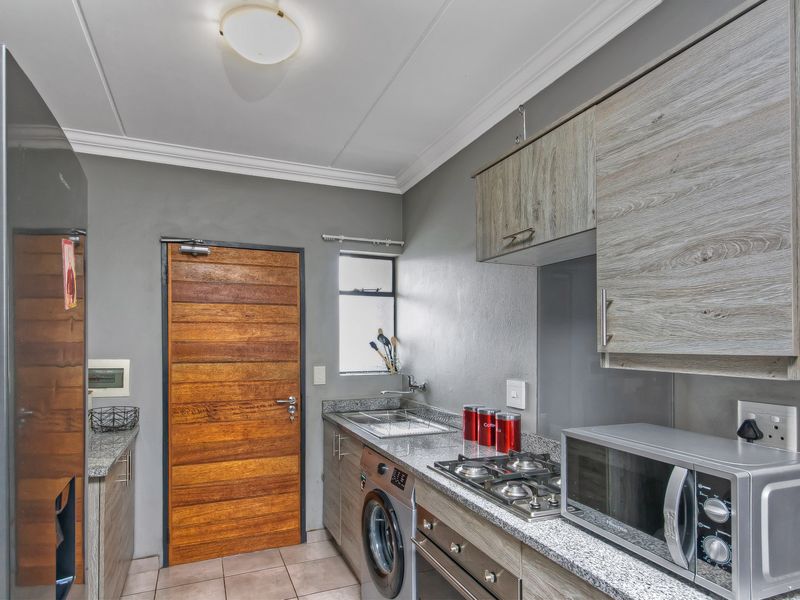 Compact kitchen featuring granite countertops, built-in cabinetry, gas hob, under-counter oven, and tiled flooring with direct access to an exterior door.