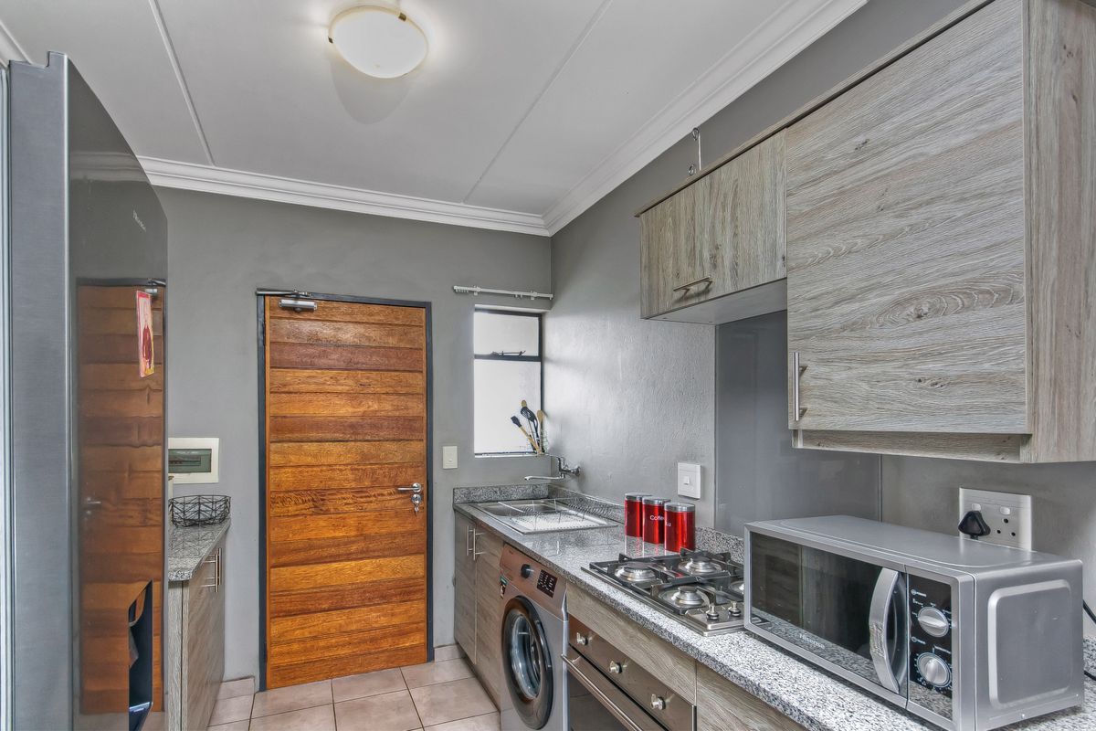 Compact kitchen featuring granite countertops, built-in cabinetry, gas hob, under-counter oven, and tiled flooring with direct access to an exterior door.