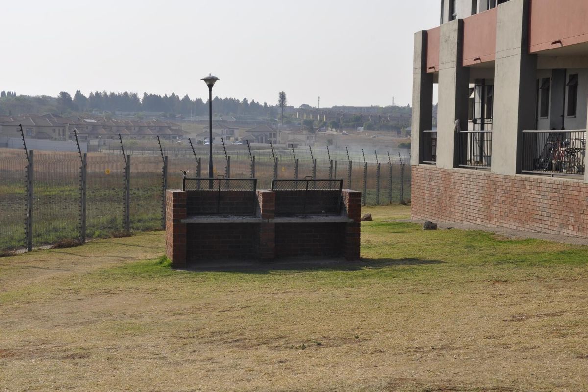 Communal outdoor area featuring a brick braai facility, lawn, and perimeter electric fencing adjacent to the apartment building.