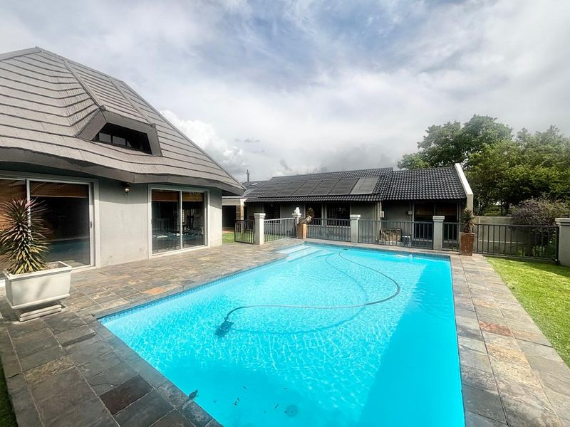 A well-maintained outdoor pool area featuring a tiled surround, metal fencing, and solar heating panels on the roof of the adjacent structure.