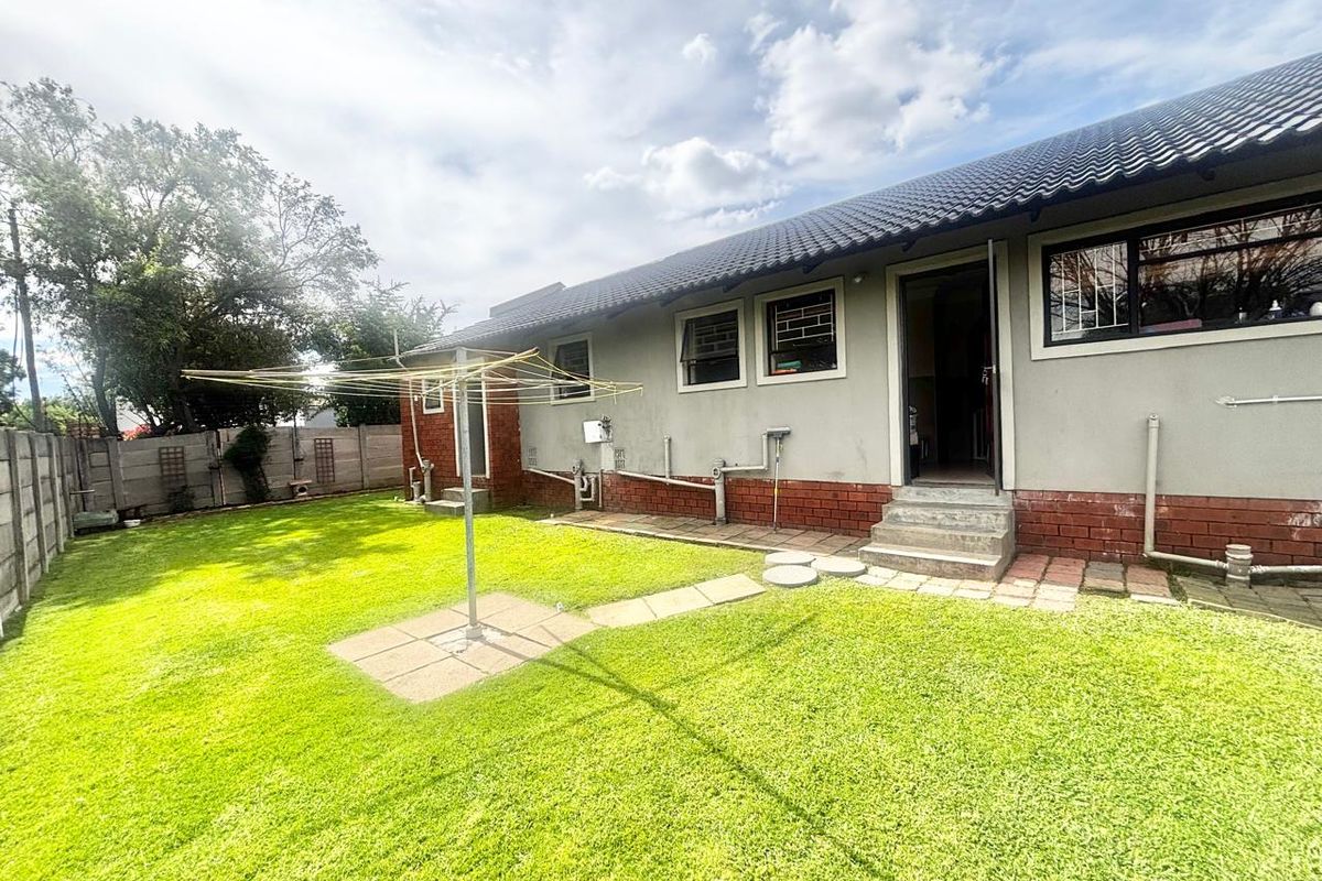 Rear view of the house featuring a lawn, concrete boundary wall, and exterior access points with security bars on windows.