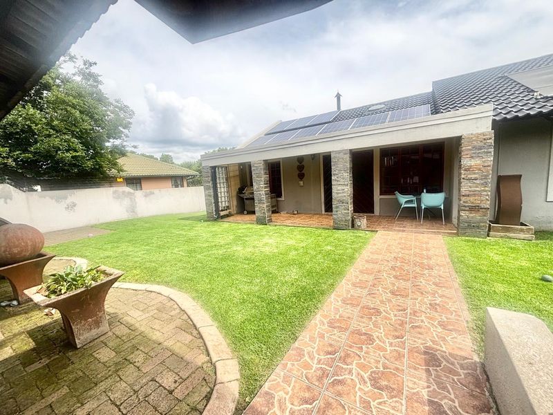 A well-maintained rear exterior featuring a covered patio with stone-clad pillars, solar panels on the roof, a paved walkway, and a neat garden.