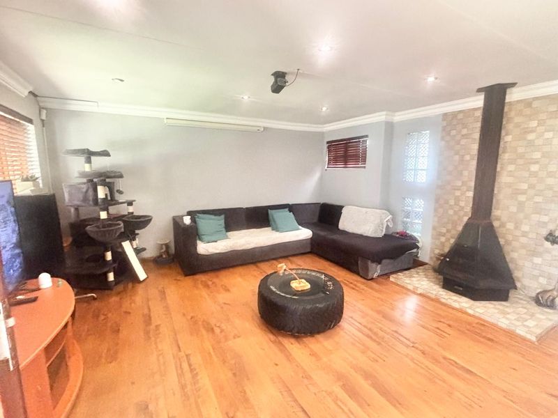 Spacious living room featuring warm timber flooring, a prominent freestanding fireplace with tiled surround, and natural light through venetian blinds.