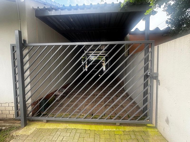 A secure, gated carport area featuring a metal sliding gate and tiled flooring, providing covered off-street parking.
